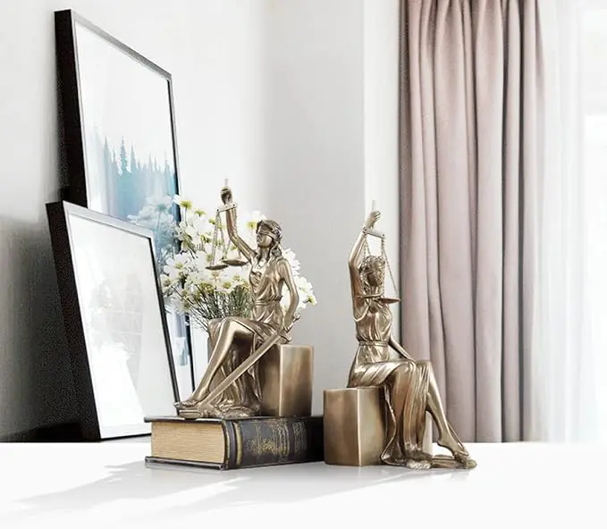 Artistic bronze sculptures of seated figures on books near a window with curtains.